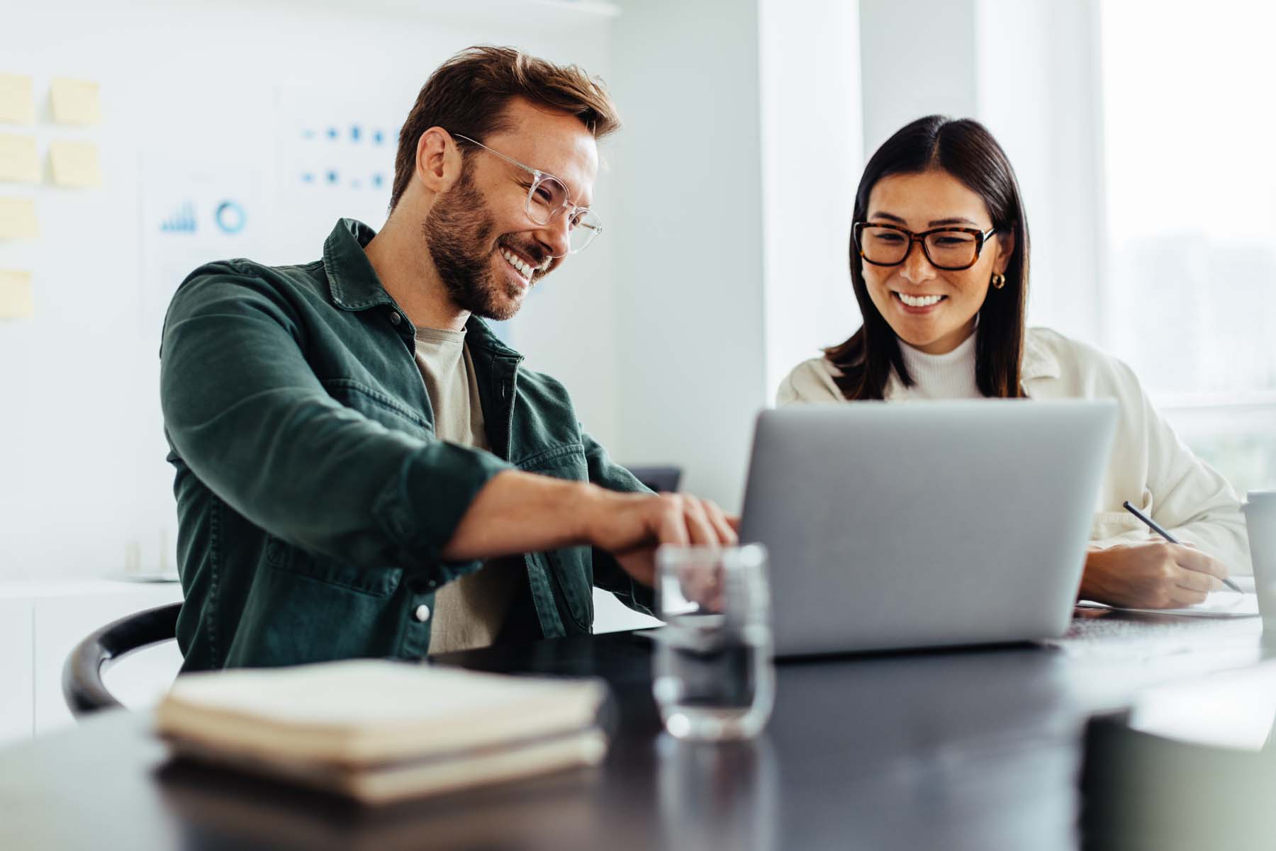 Two business people using a laptop together while sitting in a meeting. Happy business people looking at a slide presentation in an office.