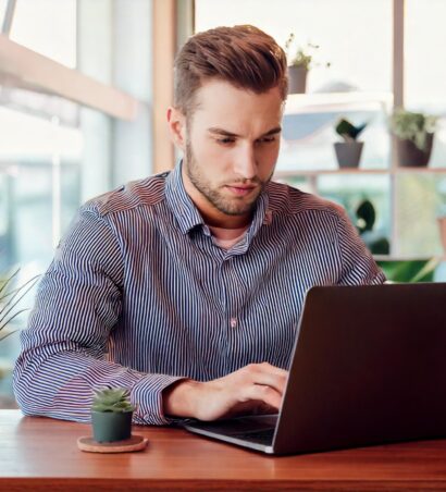 Eine einzelne Person sitzt an einem modernen Schreibtisch und arbeitet konzentriert am Laptop. . Die Umgebung ist minimalistisch und kreativ – z. B. mit einem kleinen Pflanzenarrangement, einer Tasse Kaffee und ein paar Notizen auf dem Tisch. Die Person wirkt entspannt, aber fokussiert, um den Prozess der Website-Erstellung zu symbolisieren.