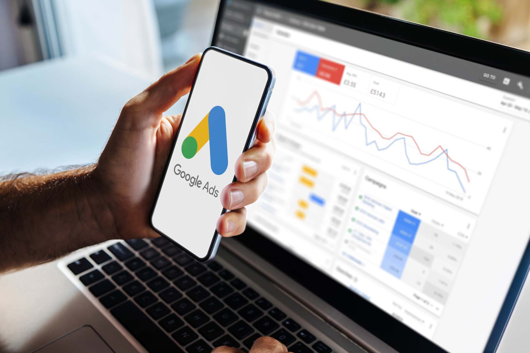 Google-Ads-Symbol auf einem Smartphone neben einem Analyse-Dashboard