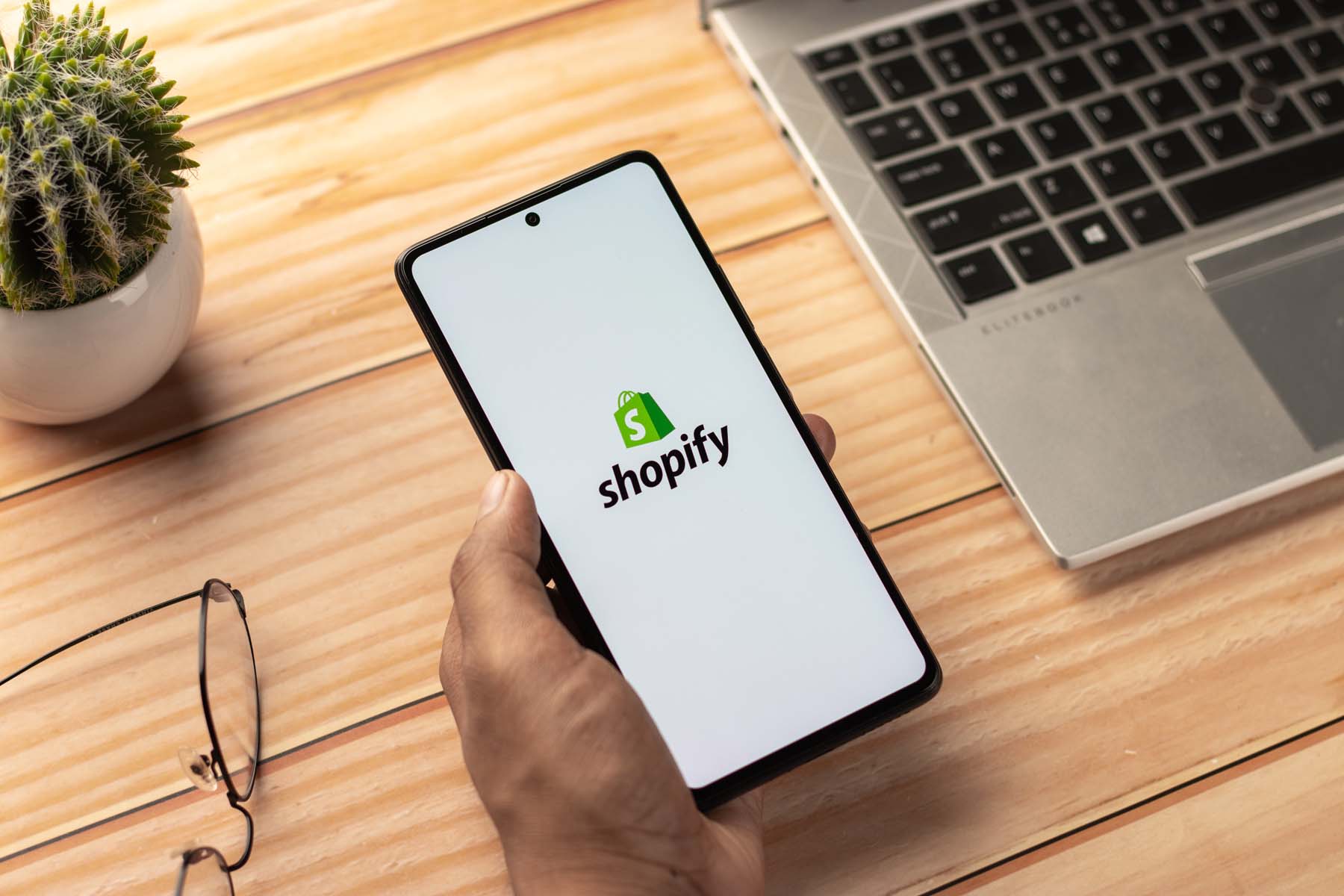 Shopify-Logo auf einem Tablet neben einem Laptop